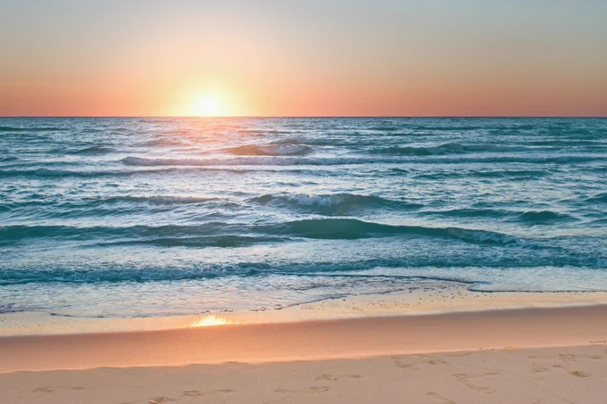 Sunset over a calm ocean, with gentle waves lapping at a sandy beach. Photo credit: iStock/Tunatura.