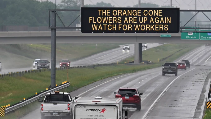 Electronic sign on highway above traffic. The sign reads, "The orange cone flowers are up again. Watch for workers.’”