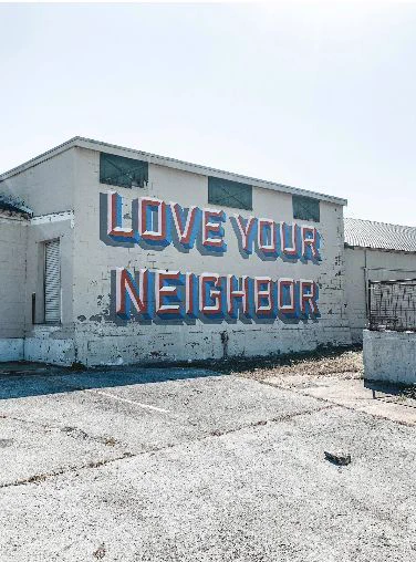"Love your neighbor" painted on a city street wall.