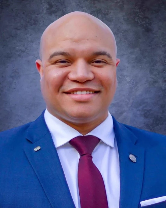 A person smiling against a blue background. They are wearing business professional clothing.