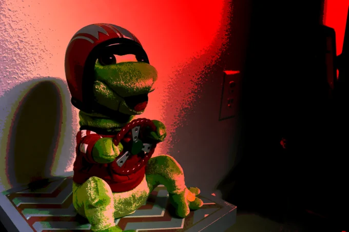 A photo of toy frog on a box wearing a helmet and holding a steering wheel, with an ominous red glow coming from the other side of the room. ✅