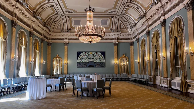 An empty banquet hall with a big chandelier and golden drapes.