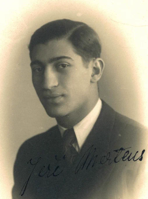 A vintage black-and-white portrait of a young person wearing a dark suit and a light-colored tie. The person has short hair, and is facing slightly to their left with a subtle smile. 