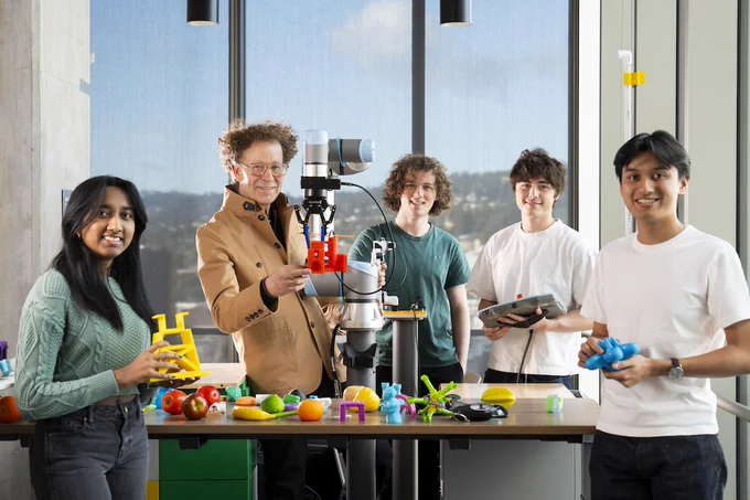 Five AUTOLab members hold multi-colored objects next to a robotic arm.
