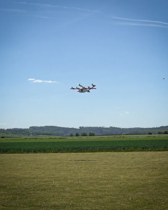 Zuri's subscale model hovering above a green field under a clear blue sky.