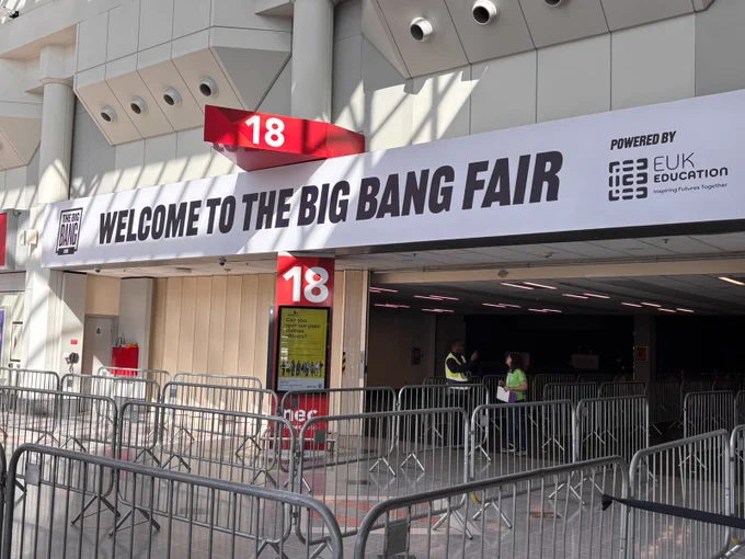 The image shows the entrance to The Big Bang Fair, with a large banner reading "Welcome to The Big Bang Fair" sponsored by EUK Education. The entrance is marked with the number 18, and barriers guide the pathway.