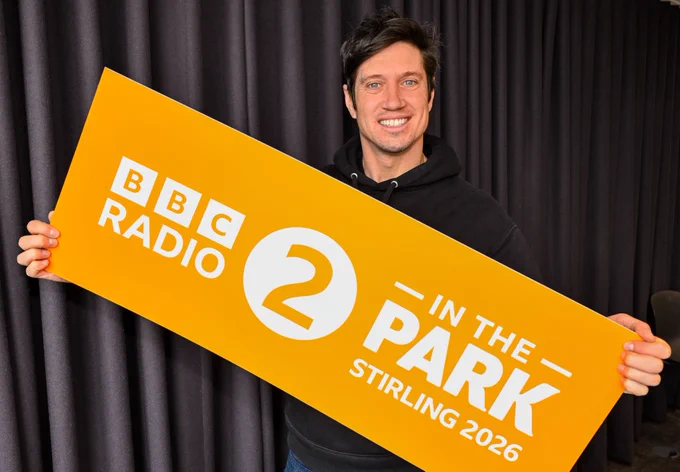 A man in a black hoodie holds a sign for BBC Radio 2 in The Park Stirling 2026