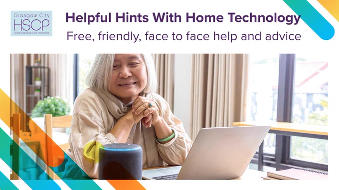 Elderly woman receiving friendly, face-to-face tech help using a laptop and smart speaker at home.