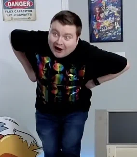 A screenshot from a live stream that shows Krazy Ken standing in the Ken Cave, making a goofy face with his eyes and mouth wide open. He's bent over slightly with his hands on his waist, but it almost looks like his arms are chicken wings or something. It's weird!