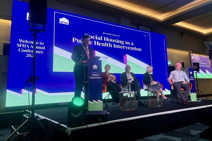 Cllr Paul Kelly presenting at the SFHA Annual Conference with panelists seated on stage.