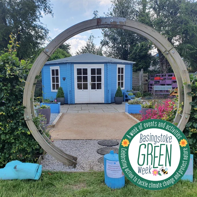 A blue garden cabin framed by a wooden arch. The Basingstoke Green Week logo is in the foreground.