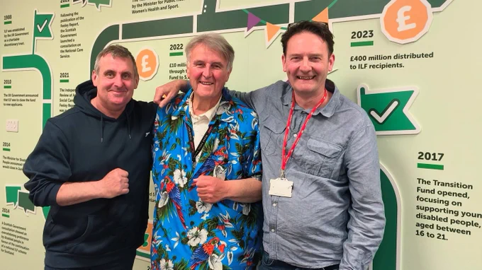 Three men in front of a timeline wall. Harvey Tilley, Jack Blaik OBE and Peter Scott OBE. They smile for the camera. Harvey and Jack appear to be about to fist bump.