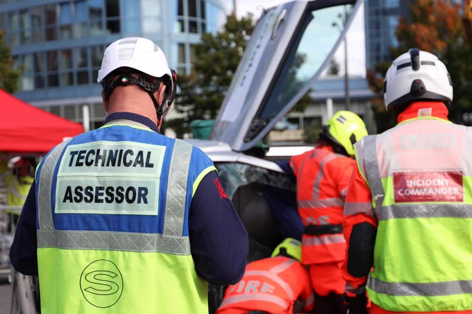 A technical assessor in full PPE watching people cutting up a car