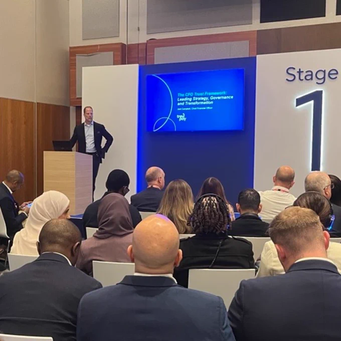 A speaker is presenting at a conference on "The CFO Trend Framework: Leading Strategy, Governance, and Transformation" at Stage 1. The audience is seated, attentively listening to the presentation.