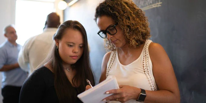 Two people engaged in a discussion while one takes notes on a notepad in a casual indoor setting.