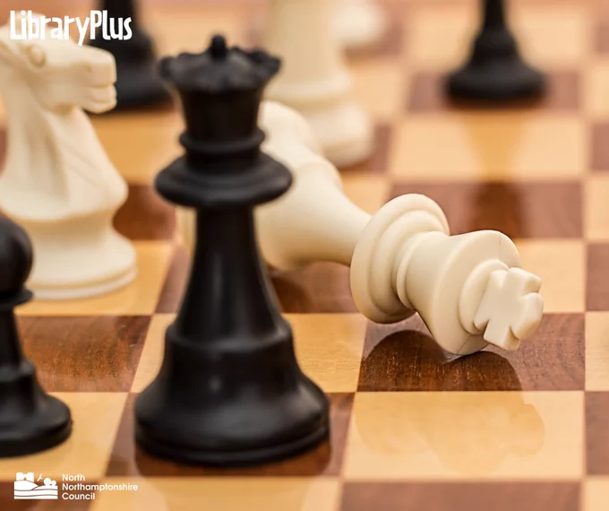 Black queen stands prominently on a wooden chessboard with a toppled white king nearby, symbolizing checkmate.