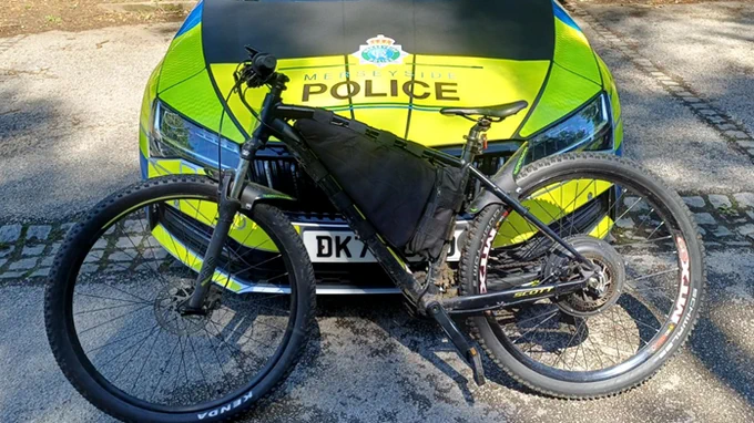 A black electric mountain bike is parked in front of a Merseyside Police car.
