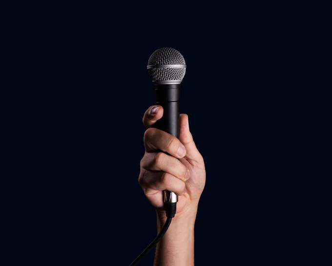 A hand holding a black microphone upright against a plain dark background.
