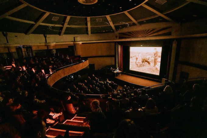 A sepia-toned low light wide shot of the Hippodrome Cinema with screen illuminated and busy audience.