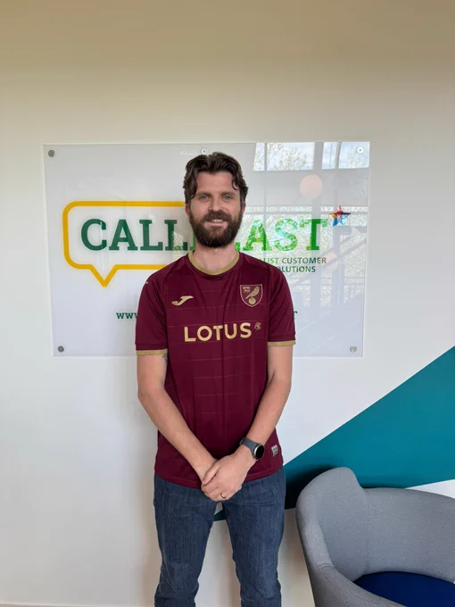 Person wearing a maroon Lotus sports jersey and jeans standing in front of a CallFast company sign indoors.