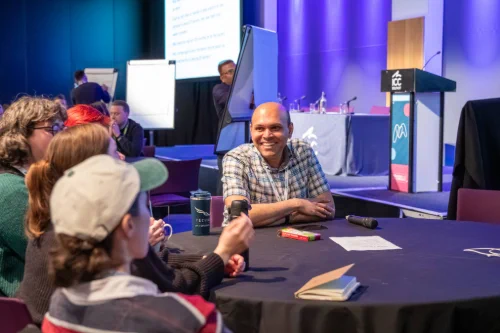 Group of people engaged in discussion around a round table at a conference with a microphone and notes on the table.