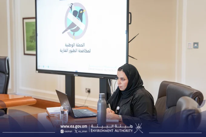 موظفة من هيئة البيئة تتابع أعمال اجتماع اللجنة الرئيسية للحملة الوطنية لمكافحة الطيور الغازية، وأمامها شاشة تعرض شعار الحملة.