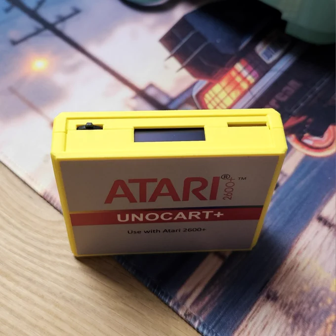 Ein Unocart  Cartridge in der Farbe gelb. Der Kamerawinkel ist schräg oben, wodurch das Label an der Front, und auch das kleine Display auf der Stirnseite sichtbar sind. 