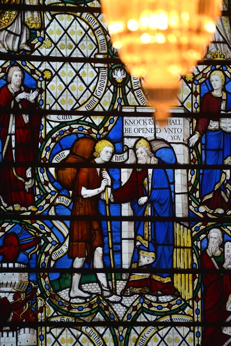 A panel of a stained glass window with a scene from John Bunyan's The Pilgrim's Progress