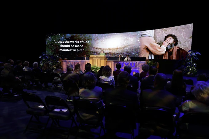 Dr. Jennifer Brooks speaks at BYU Devotional. A large screen behind her shows an image of Jesus Christ healing a blind man.