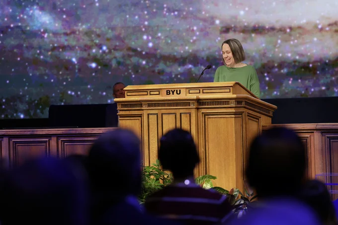 Dr. Jennifer Brooks smiles as she speaks at a podium at BYU Devotional, June 2026