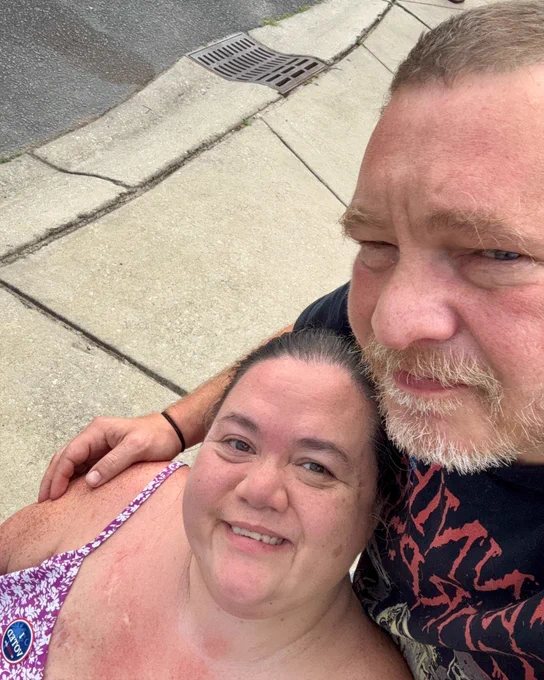  Angel, a biracial Korean and white person in a wheelchair, takes a selfie with their husband, sporting the sticker.