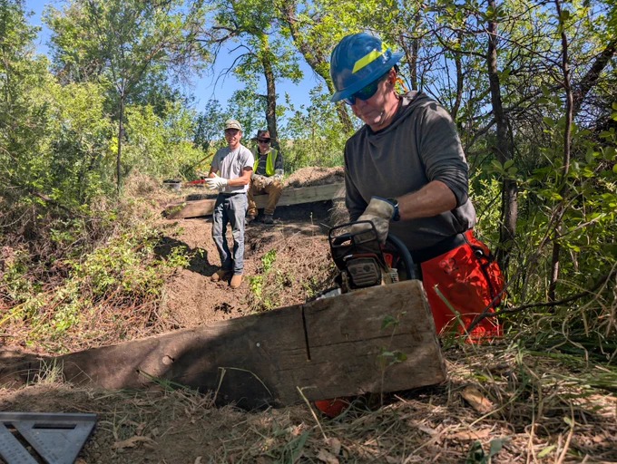 In the foreground, Jeff Davis, DPG trails manager, uses a chainsaw to cut a beam for the bridge construction project. Forest Service photo by Scott C. Marvin