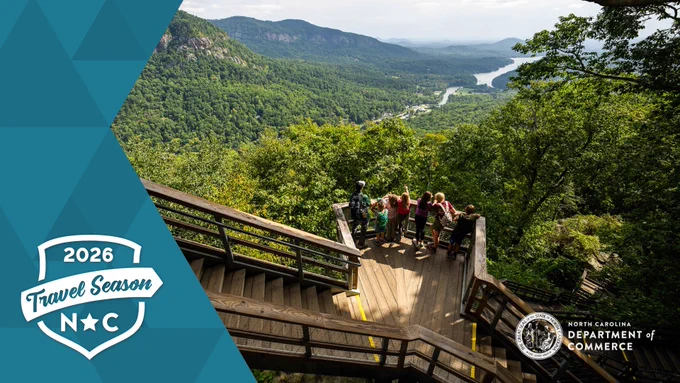 Hikers at Chimney Rock with an overlay of the "2026 Travel Season NC" badge and N.C. Commerce logo.