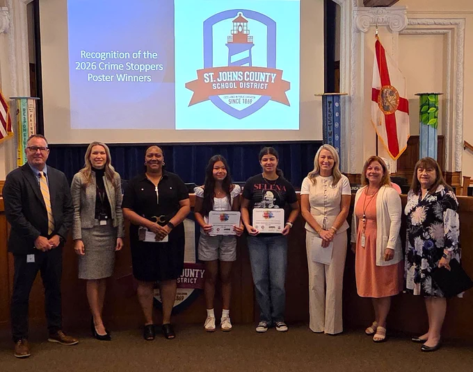 Group photo of St. Johns County School District officials and two middle school students holding Crime Stoppers poster awards.