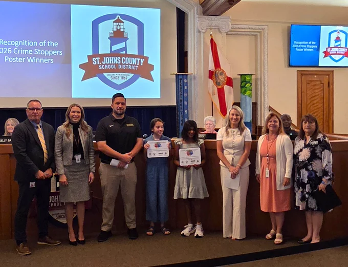 Group photo of St. Johns County School District officials and two elementary students holding Crime Stoppers poster awards.
