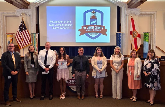 Group photo of St. Johns County School District officials and two high school students holding Crime Stoppers poster awards.