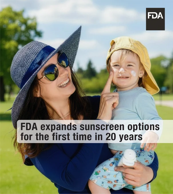 A person wearing a sunhat and sunglasses holds a child with a yellow hat, who has sunscreen on their face. Both are smiling outdoors on a sunny day. The image includes a text overlay: "FDA expands sunscreen options for the first time in 20 years." The FDA logo is in the top right corner.