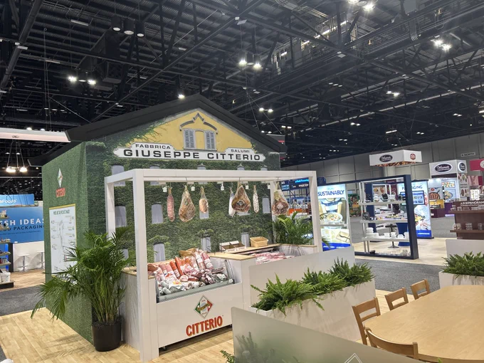 A trade show booth showcasing cured meats from Giuseppe Citterio. The booth is designed like a small deli with hanging meats and product displays.