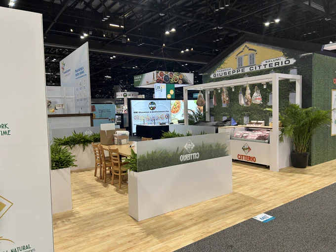 A trade show booth showcasing Citterio products with hanging meats and an inviting seating area. The atmosphere is professional and organized.