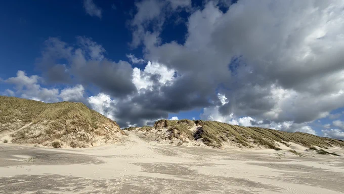 Blick über den Strand in Richtung Dünen mit dramatischem Wolkenhimmel