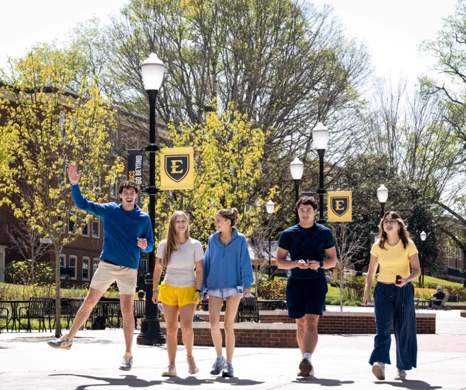 Group of 5 cheerful-looking ETSU students walking towards the ETSU D.P. Culp Center with ETSU banners behind them.