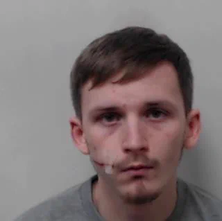 Image of man with short brown hair wearing a grey top. Has a laceration along the side of his face from corner of mouth with tape over it.