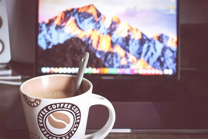 An image of a coffee cup in front of a laptop screen