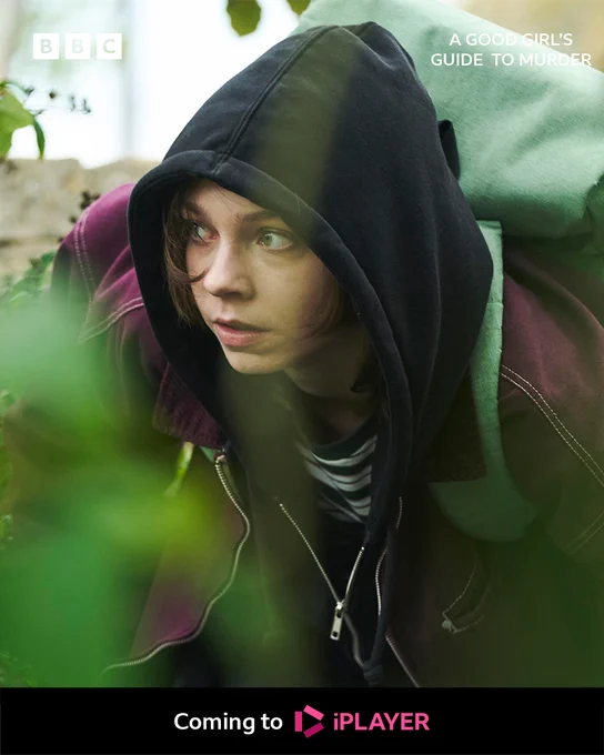 Pip crouching hiding behind a bush with her hood up 