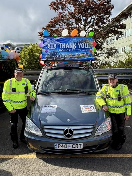 Two police officers stand with a taxi decorated with a "Thank You Police Scotland" banner and balloons.