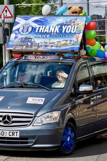 A taxi decorated with a "Thank You Police Scotland" banner and balloons, with a teddy bear on top.