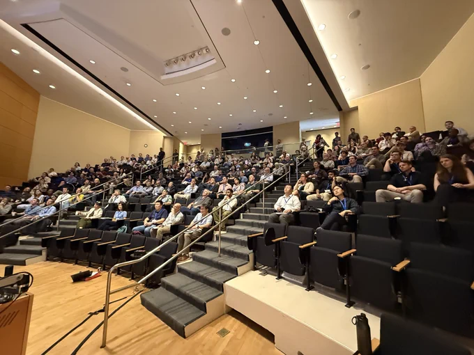 A view from the speaker's perspective of a full lecture hall, with attendees visibly engaged and attentive.