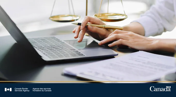 Person using a laptop and holding a pen with legal scales in the background on a desk with documents.