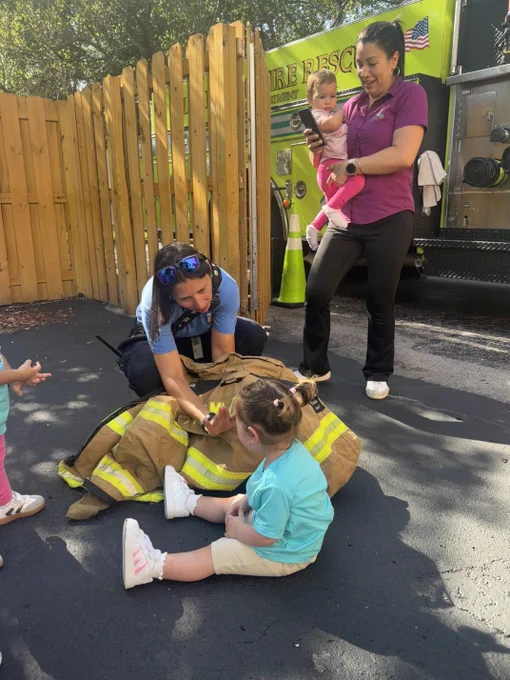 Children from a preschool participate in a Miami-Dade Fire Rescue Community Affairs visit, exploring a fire truck, viewing firefighting gear, and interacting with team members during a fire safety presentation.