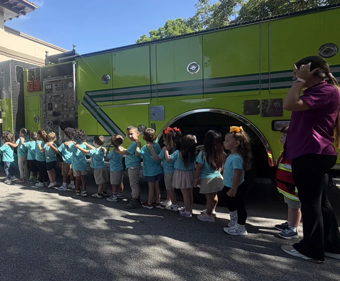 Children from a preschool participate in a Miami-Dade Fire Rescue Community Affairs visit, exploring a fire truck, viewing firefighting gear, and interacting with team members during a fire safety presentation.
